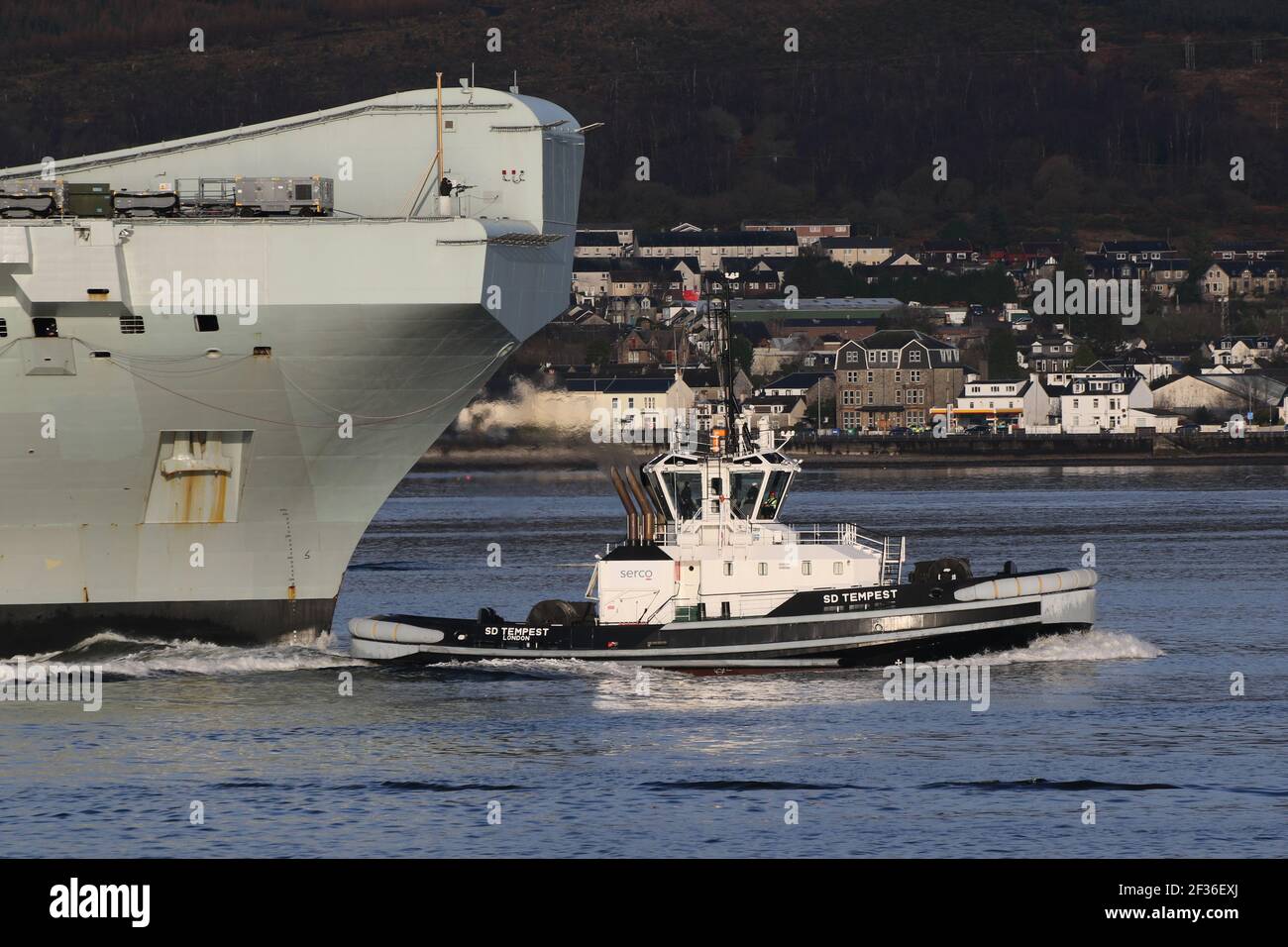 SD Tempest, a Damen ART 8032 tug boat operated by Serco Marine Services, is seen here escorting the Royal Navy aircraft carrier HMS Queen Elizabeth (R08) on the carrier's first visit to the Firth of Clyde. Stock Photo
