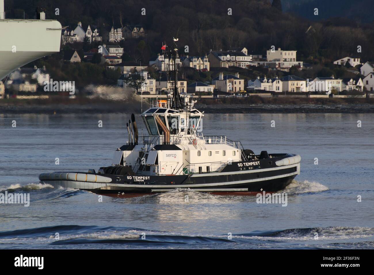 SD Tempest, a Damen ART 8032 tug boat operated by Serco Marine Services, is seen here escorting the Royal Navy aircraft carrier HMS Queen Elizabeth (R08) on the carrier's first visit to the Firth of Clyde. Stock Photo