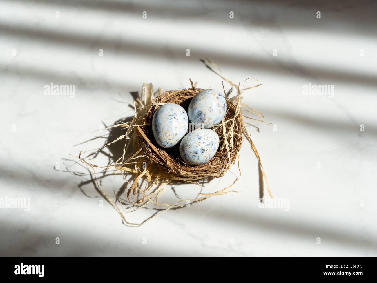 Three small Easter blue eggs in the nest, beautiful background with shadows Stock Photo