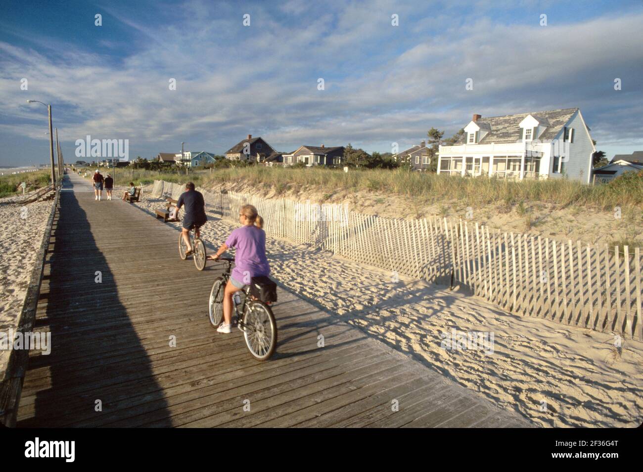 Delaware Rehoboth Beach boardwalk bicycles biking riding man woman female couple,public beach rental vacation cottages Atlantic Ocean seashore Stock Photo