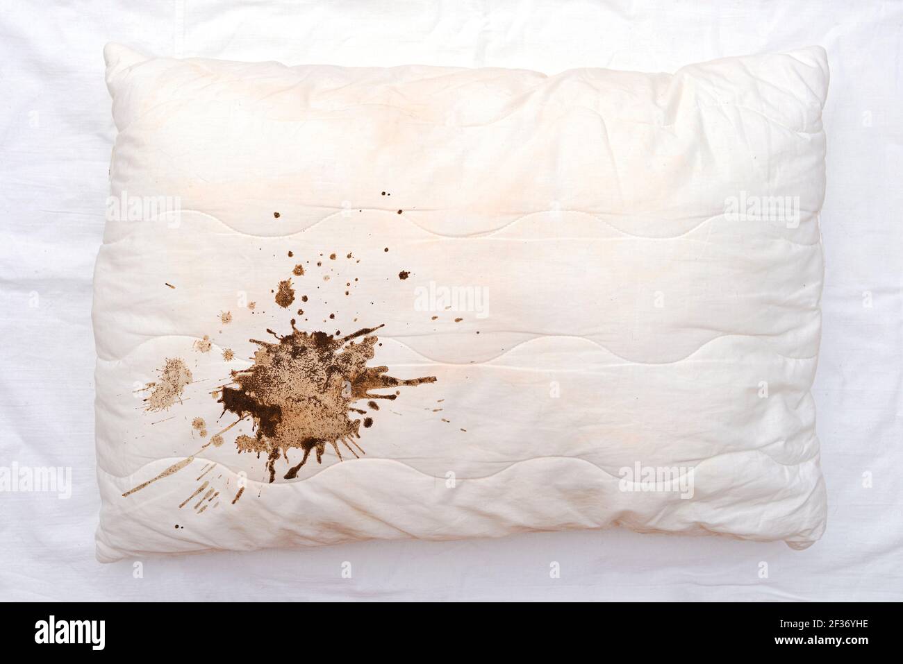 Old used white pillow with stains on crumpled sheet, dirty pillow on