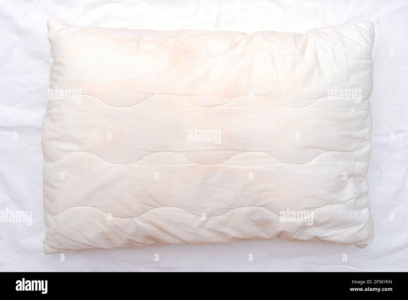 Old used white pillow with stains on crumpled sheet, dirty pillow on