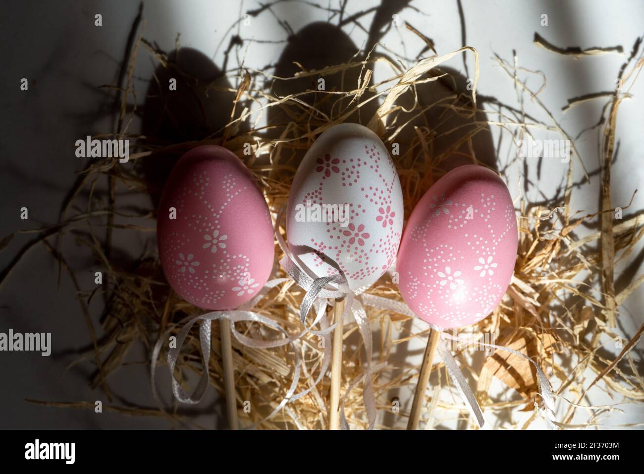 Two pink eggs and one white in the hay, beautiful background with shadows Stock Photo