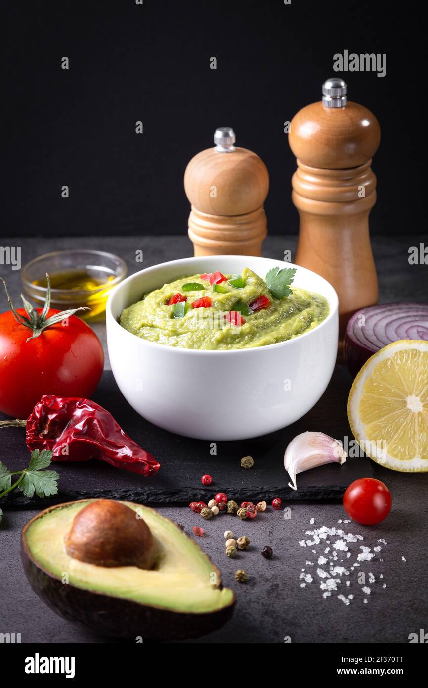 Bowl of guacamole and ingredients on dark background  vertical format Stock Photo