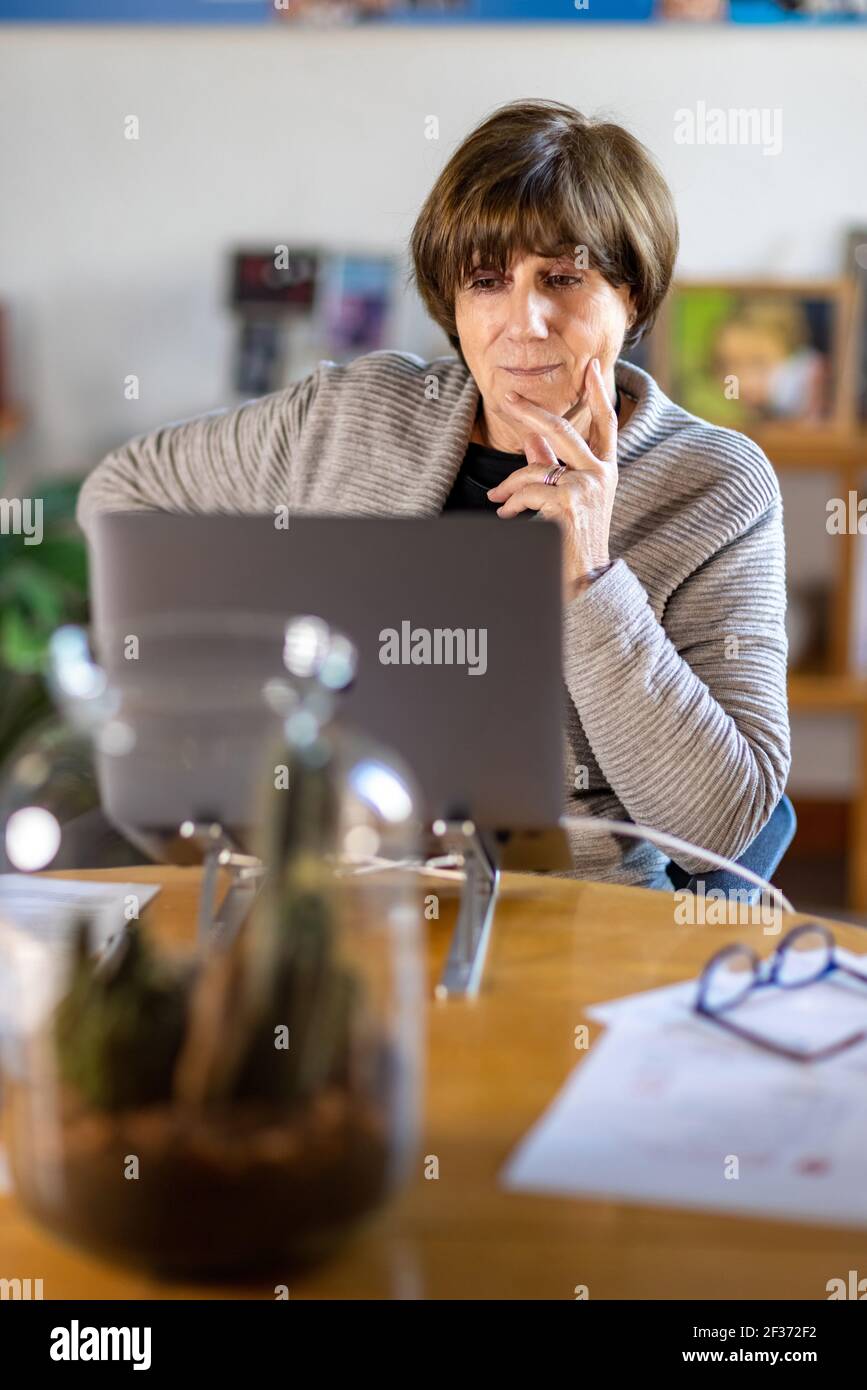 Elderly Psychologist and Senior Consultant working remotely from home during a video meeting with her laptop during quarantine or lockdown Stock Photo