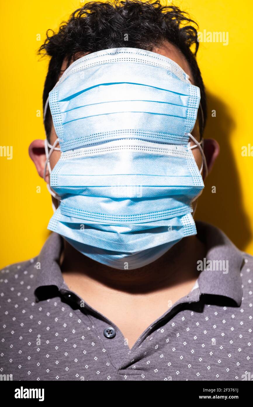 Surgical masks cover unrecognizable person's face against yellow background Stock Photo