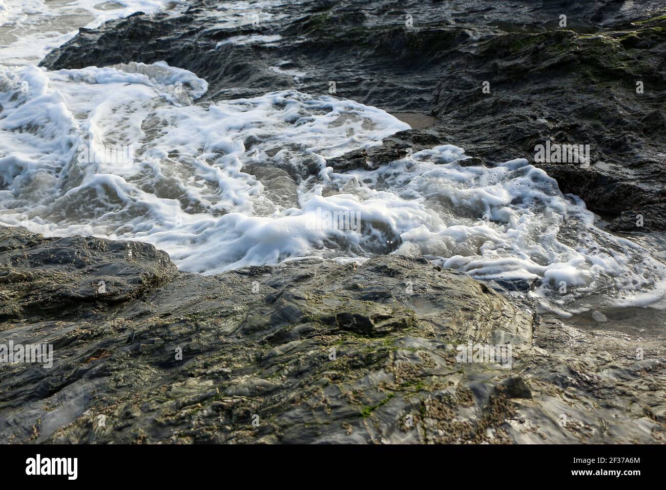 Waves crashing over rocks and up onto the Carlyon Bay beach outside St Austell, Cornwall, England following a storm far out to sea in the Atlantic oce Stock Photo