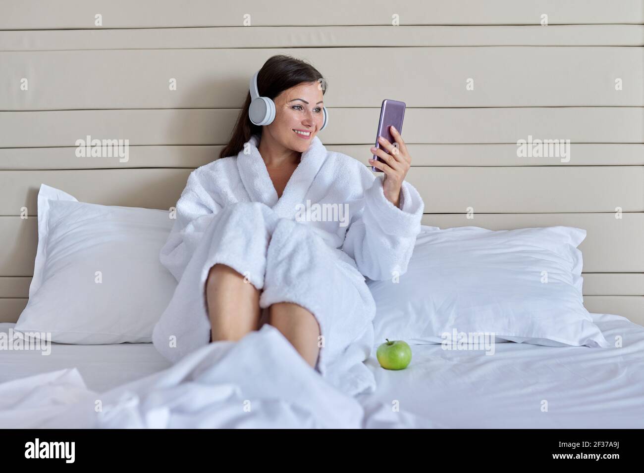 Happy talking mature woman in headphones using smartphone for video ...