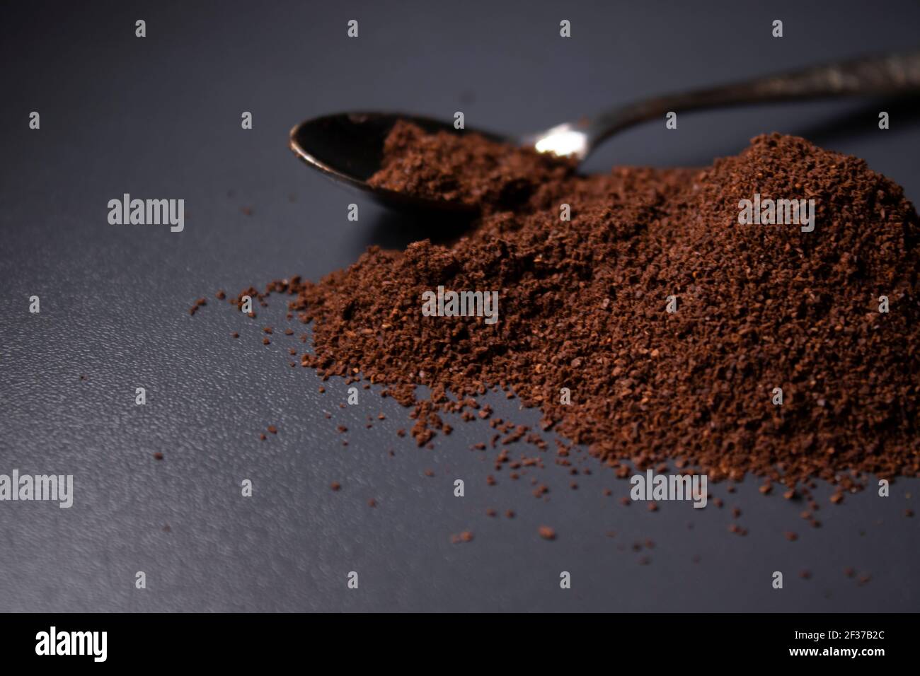 gold teaspoon in a pile of ground or instant coffee on dark background