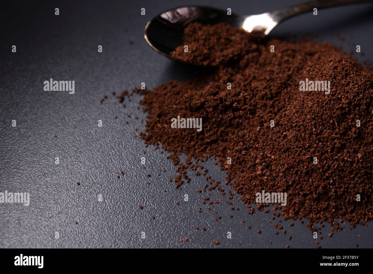 gold teaspoon in a pile of ground or instant coffee on dark background