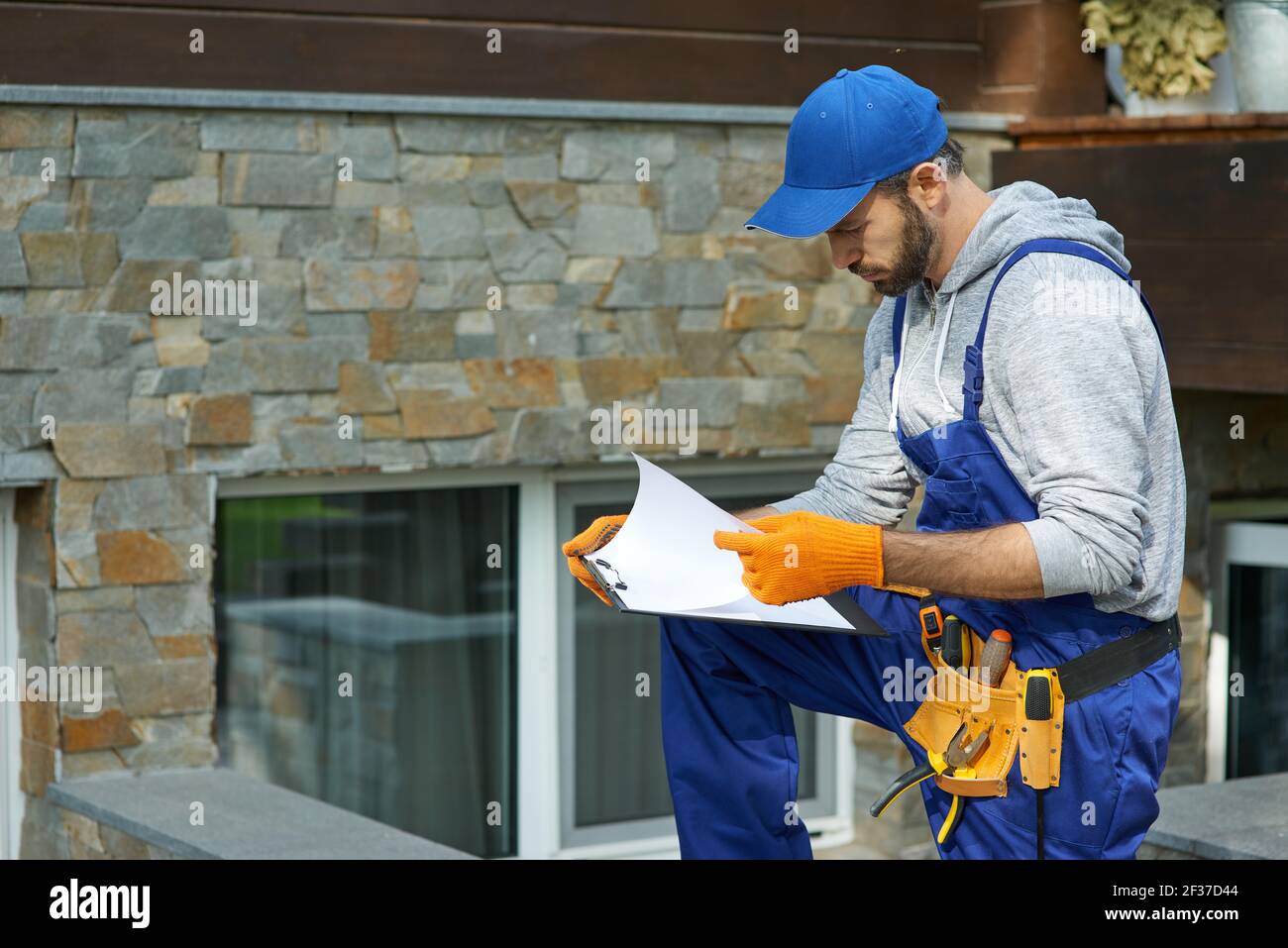 Young workman in uniform looking focused, standing outdoors with papers while working on construction project Stock Photo