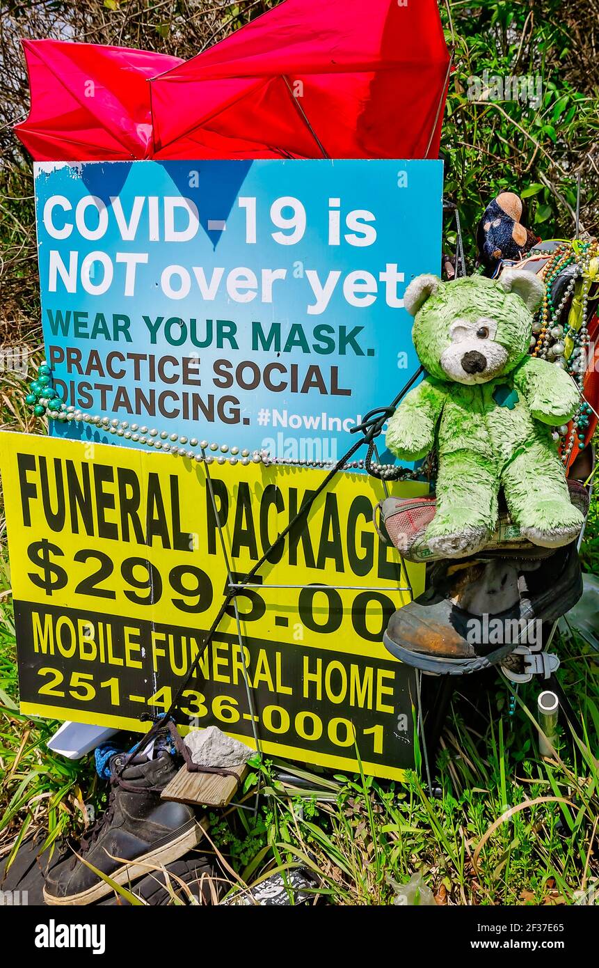 A roadside memorial art display includes a sign about COVID-19, a funeral home advertisement, and other items in Prichard, Alabama. Stock Photo