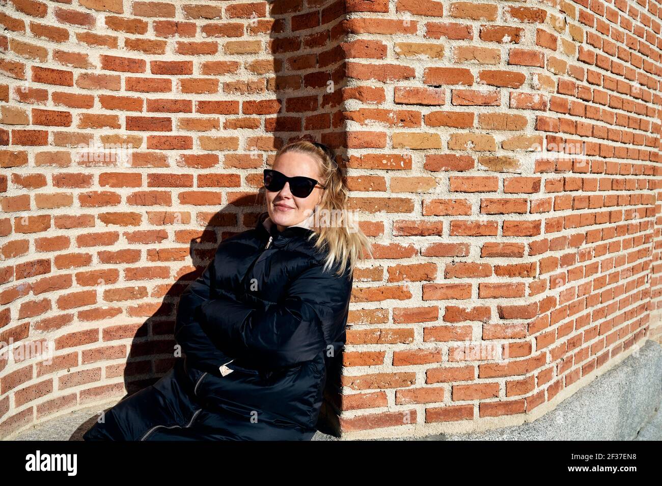 Woman in outerwear leaning on brick wall Stock Photo