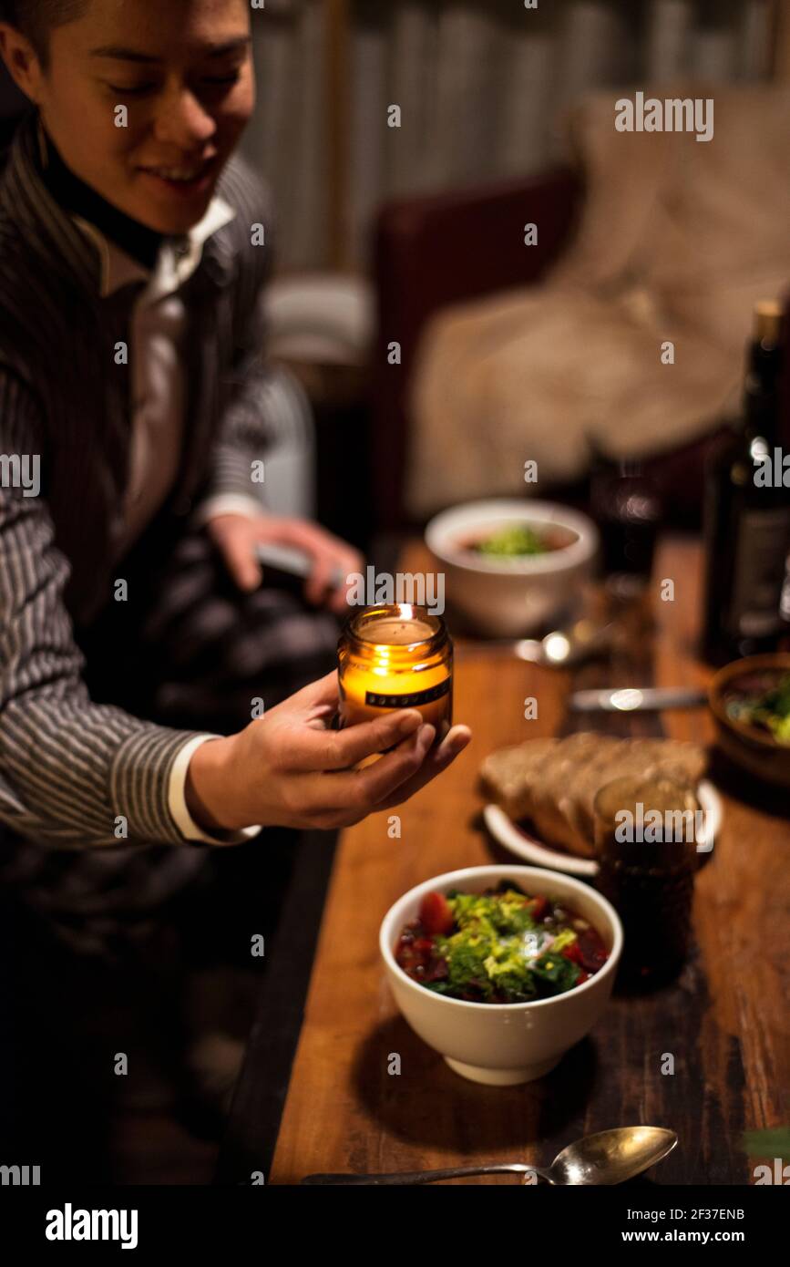 queer person smiles and places candle at dinner table at night Stock Photo