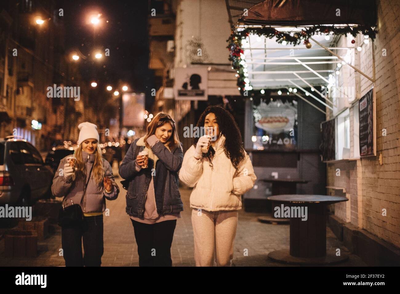 Young women with disposable cups walking on street in city at night Stock Photo