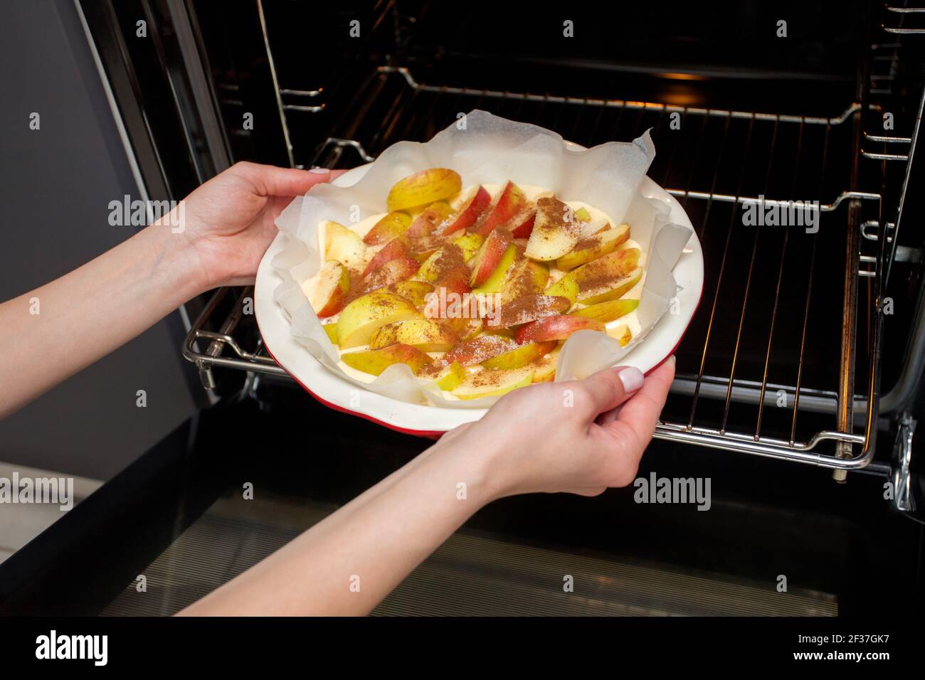The hostess prepares apple charlotte at home in the kitchen and puts in the oven an apple pie Stock Photo