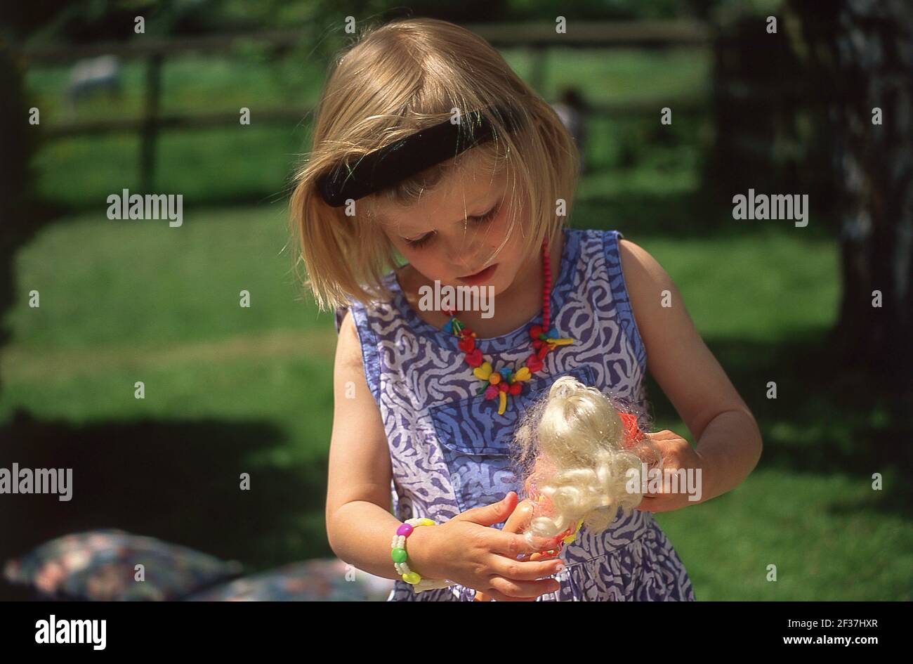 Young girl playing with Barbie doll, in garden, Winkfield, Berkshire, England, United Kingdom Stock Photo