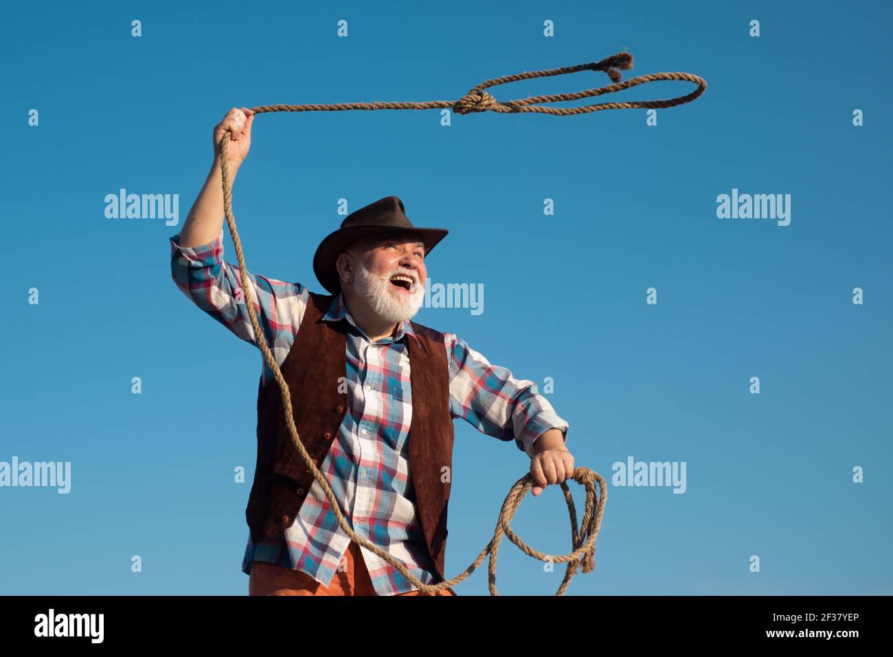 Old wild west cowboy with rope. Bearded western man throwing lasso with  brown jacket and hat catching horse or cow Stock Photo - Alamy