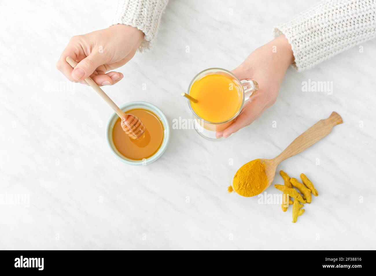 Woman making healthy turmeric drink with honey on light background
