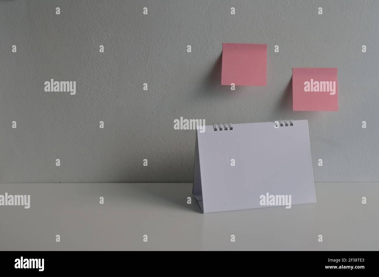 Closeup and selective focus on blank desk calendar standing on wooden table against empty sticky notes on cement wall Stock Photo