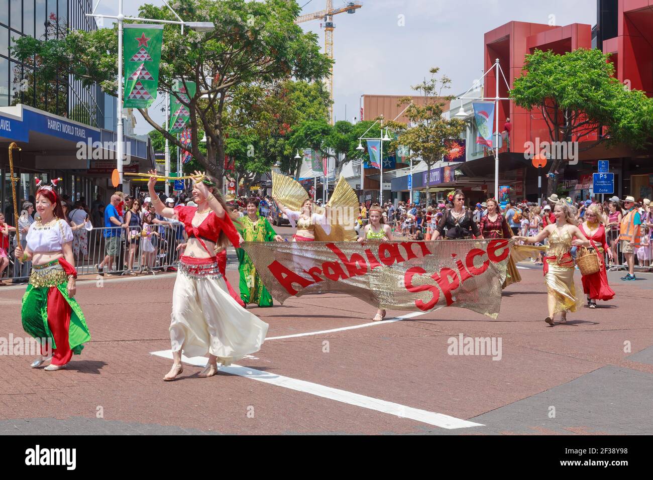 Belly dancers in colorful outfits and with an 'Arabian Spice' banner walking down the street during a Christmas parade in Tauranga, New Zealand Stock Photo