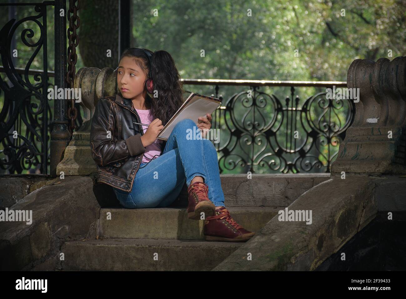 Teenager is sitting on the steps of a park, she writes notes in her ...