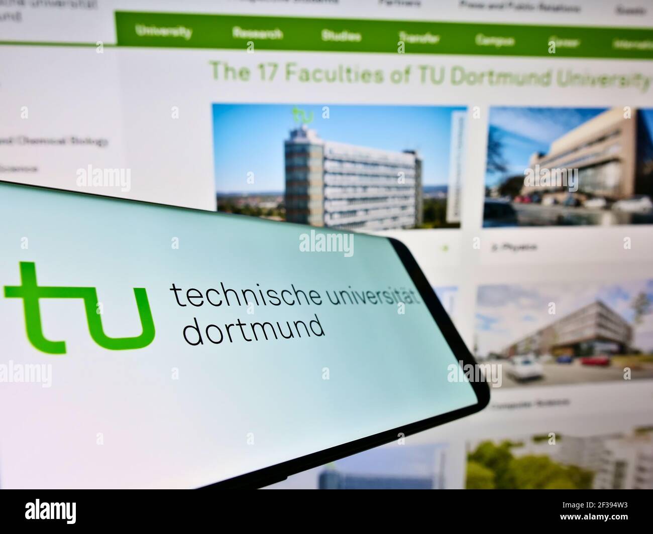 Smartphone with logo of German education institution Technical University of Dortmund on screen in front of website. Focus on center of phone display. Stock Photo