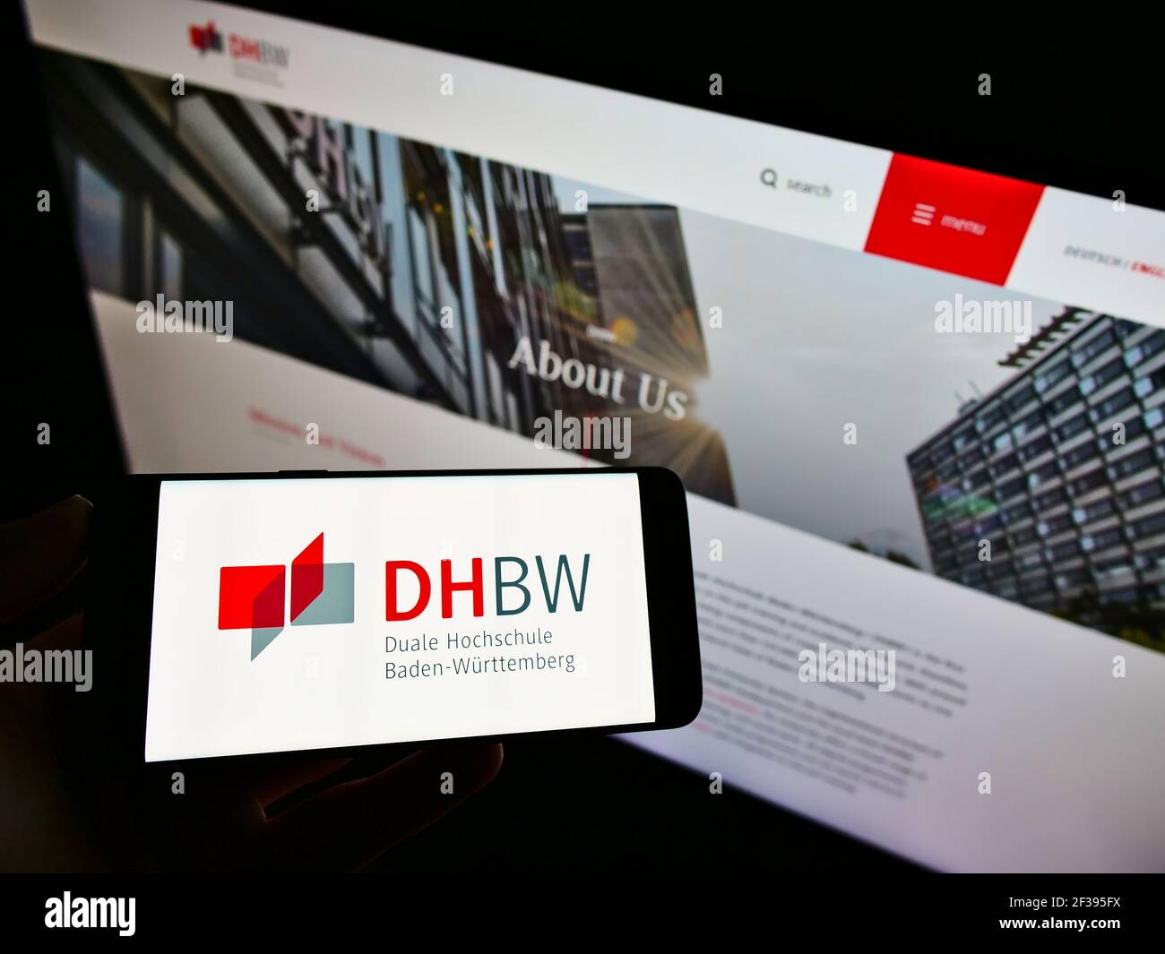 Person holding smartphone with logo of German Duale Hochschule Baden-Württemberg (DHBW) on screen in front of website. Focus on phone display. Stock Photo