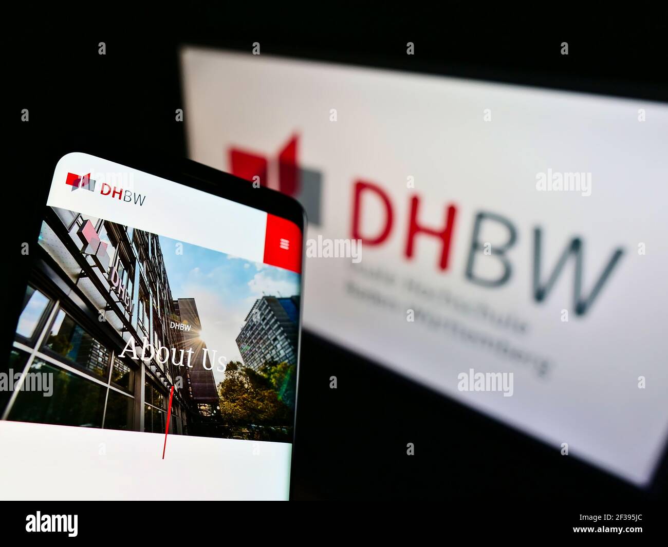 Mobile phone with website of German Duale Hochschule Baden-Württemberg (DHBW) on screen in front of logo. Focus on top-left of phone display. Stock Photo