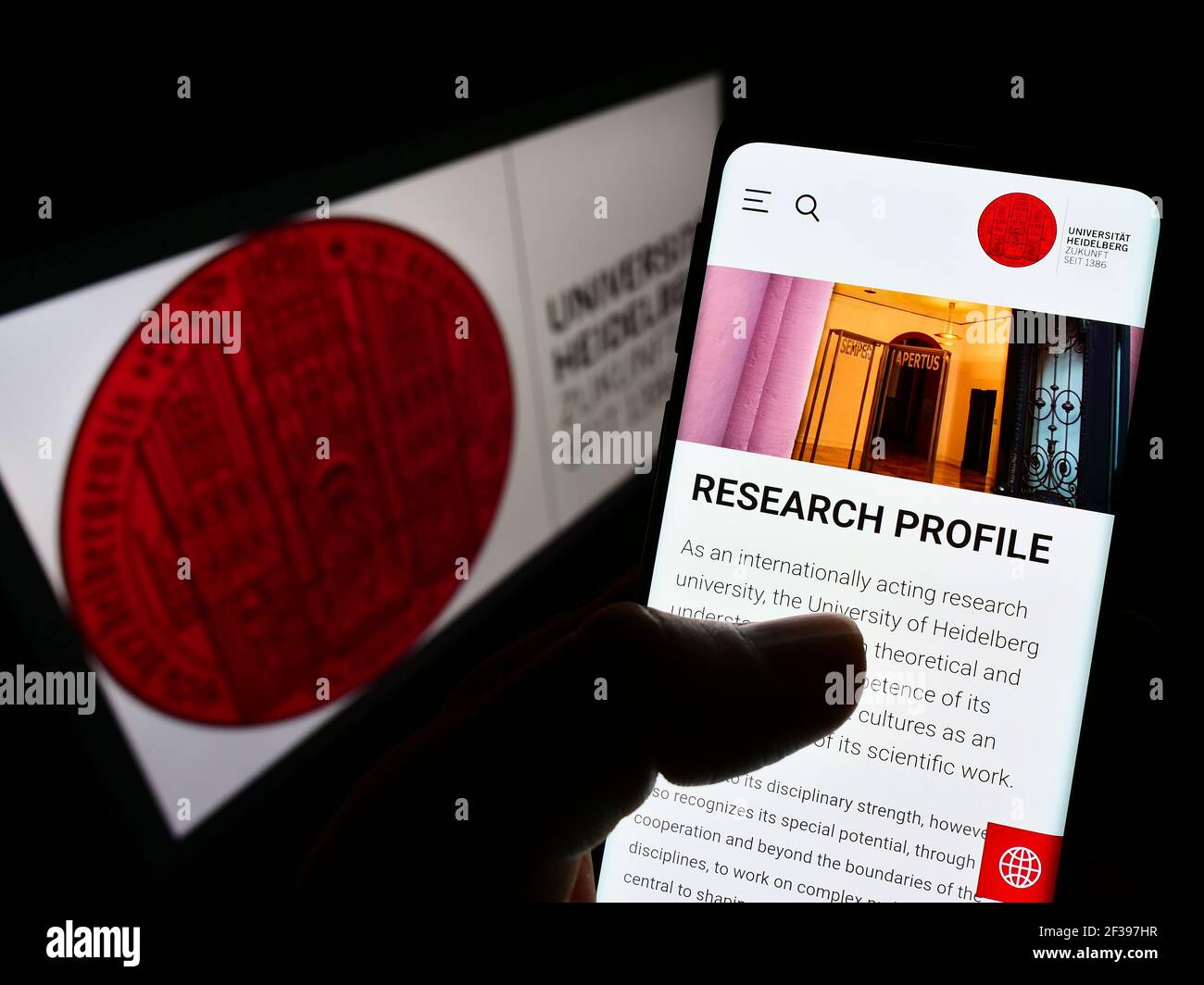 Person holding cellphone with webpage of German Heidelberg University on screen in front of logo. Focus on center of phone display. Unmodified photo. Stock Photo