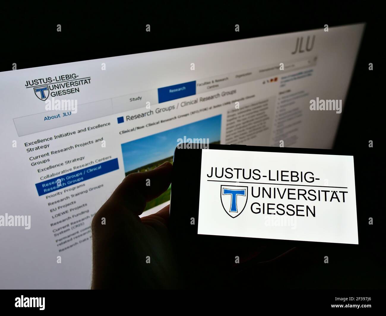 Person holding smartphone with logo of German university Justus-Liebig-Universität Gießen on screen in front of website. Focus on phone display. Stock Photo