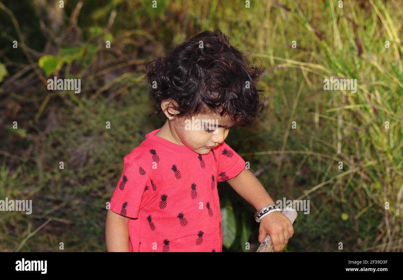 Portrait photo of a small Indian child playing with wood in the garden, india. concept for Childhood memories, smile on young child's face, children p Stock Photo