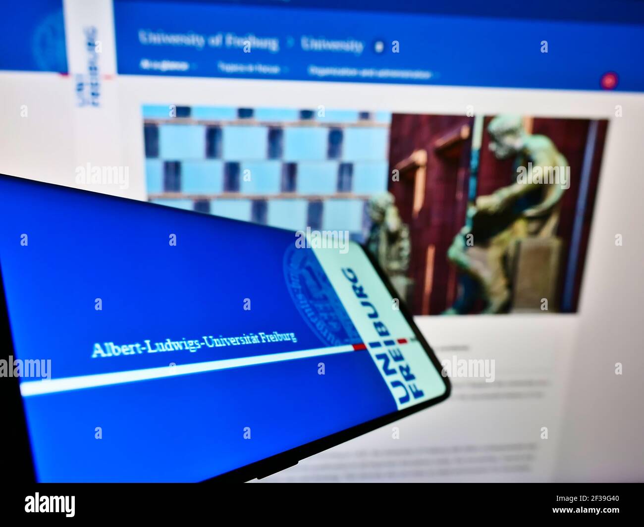 Cellphone with logo of German education institution University of Freiburg on screen in front of website. Focus on center-right of phone display. Stock Photo