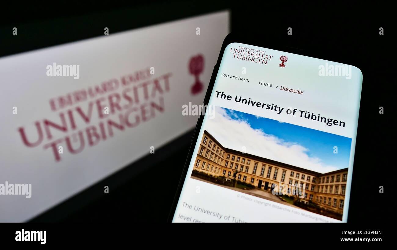 Person holding cellphone with web page of German University of Tübingen on screen in front of logo. Focus on top-left of phone display. Stock Photo