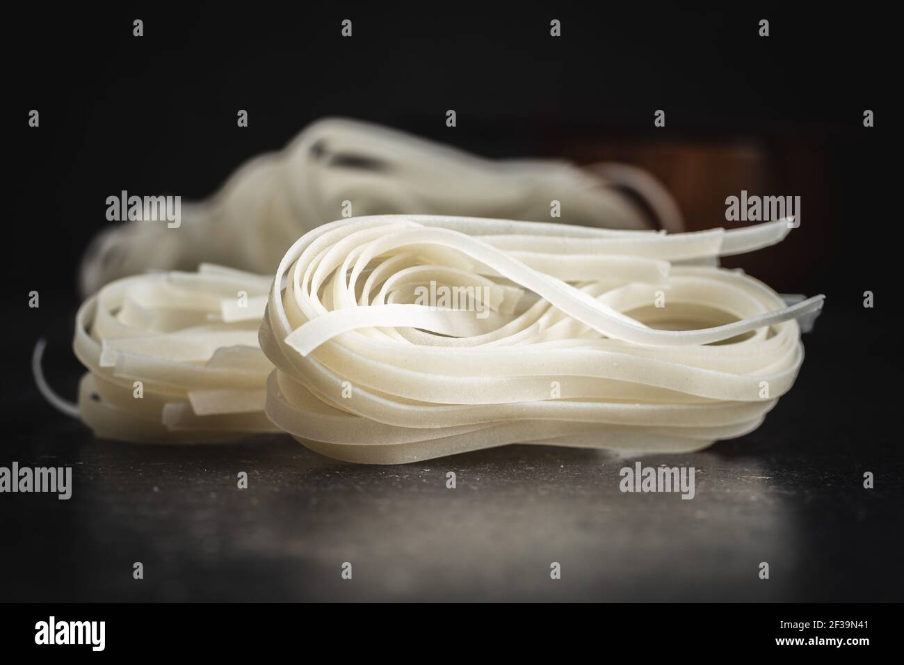 Dried white rice noodles. Raw pasta. Uncooked noodles on black table. Stock Photo