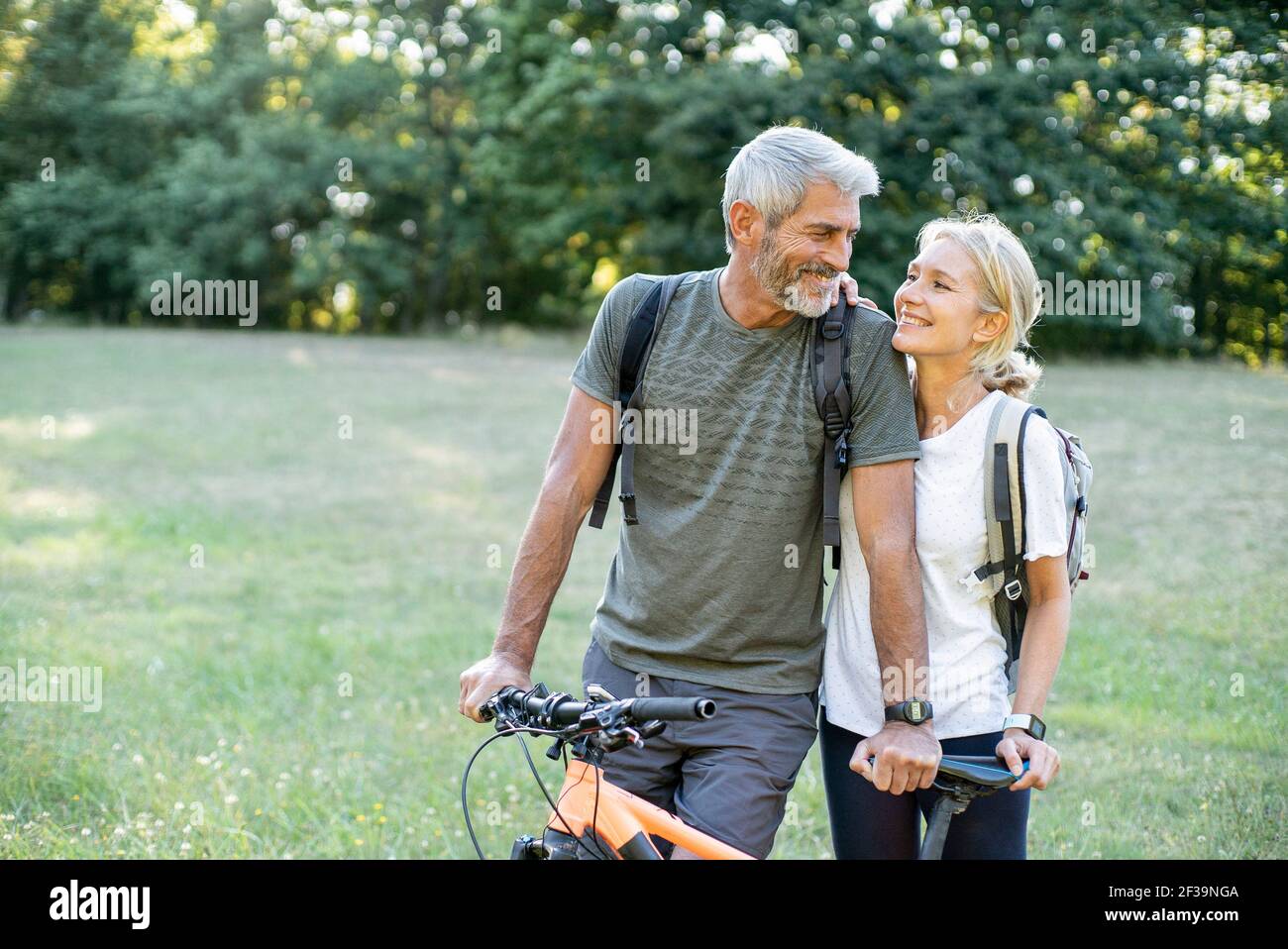 Smiling mature couple with bicycle looking at each other in forest Stock Photo