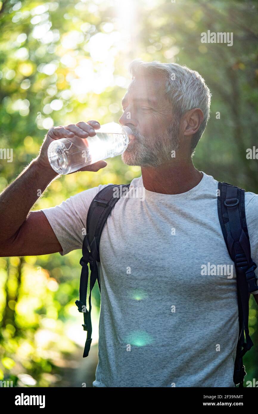 Mature man drinking water in forest on sunny day Stock Photo