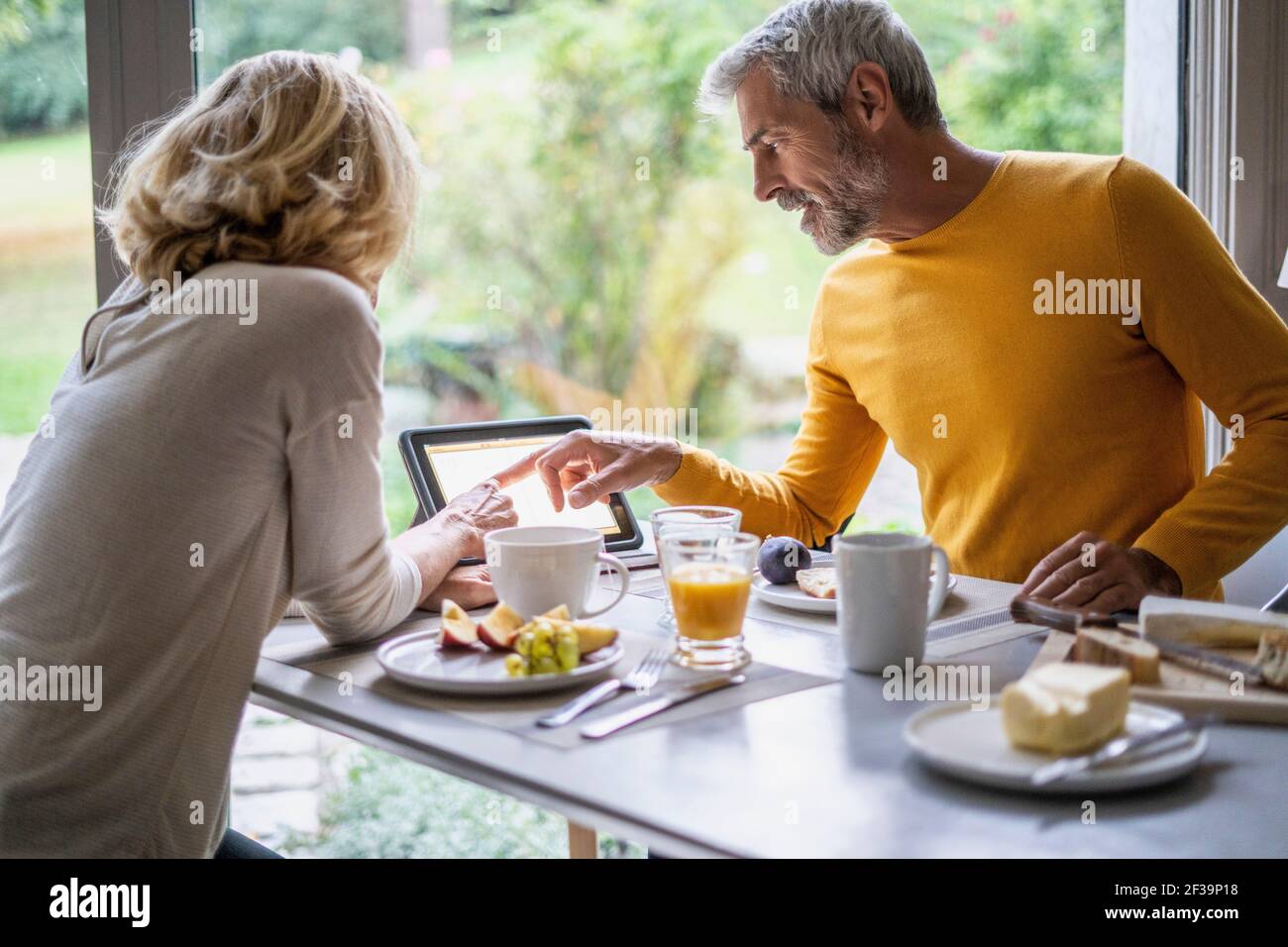 Mature couple using digital tablet while having breakfast at home Stock Photo