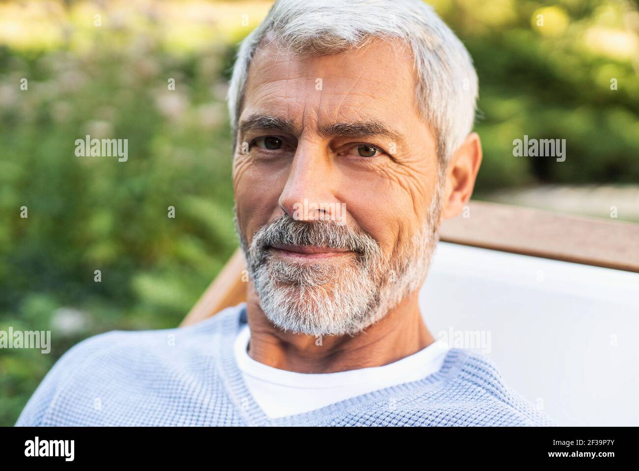 Portrait of smiling mature man sitting in backyard Stock Photo
