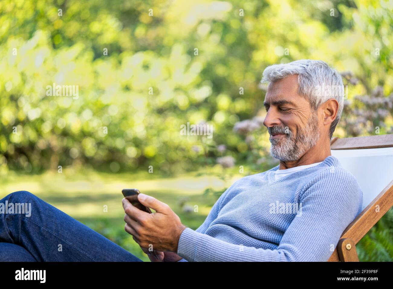 Smiling mature man using smartphone while sitting on deckchair Stock Photo