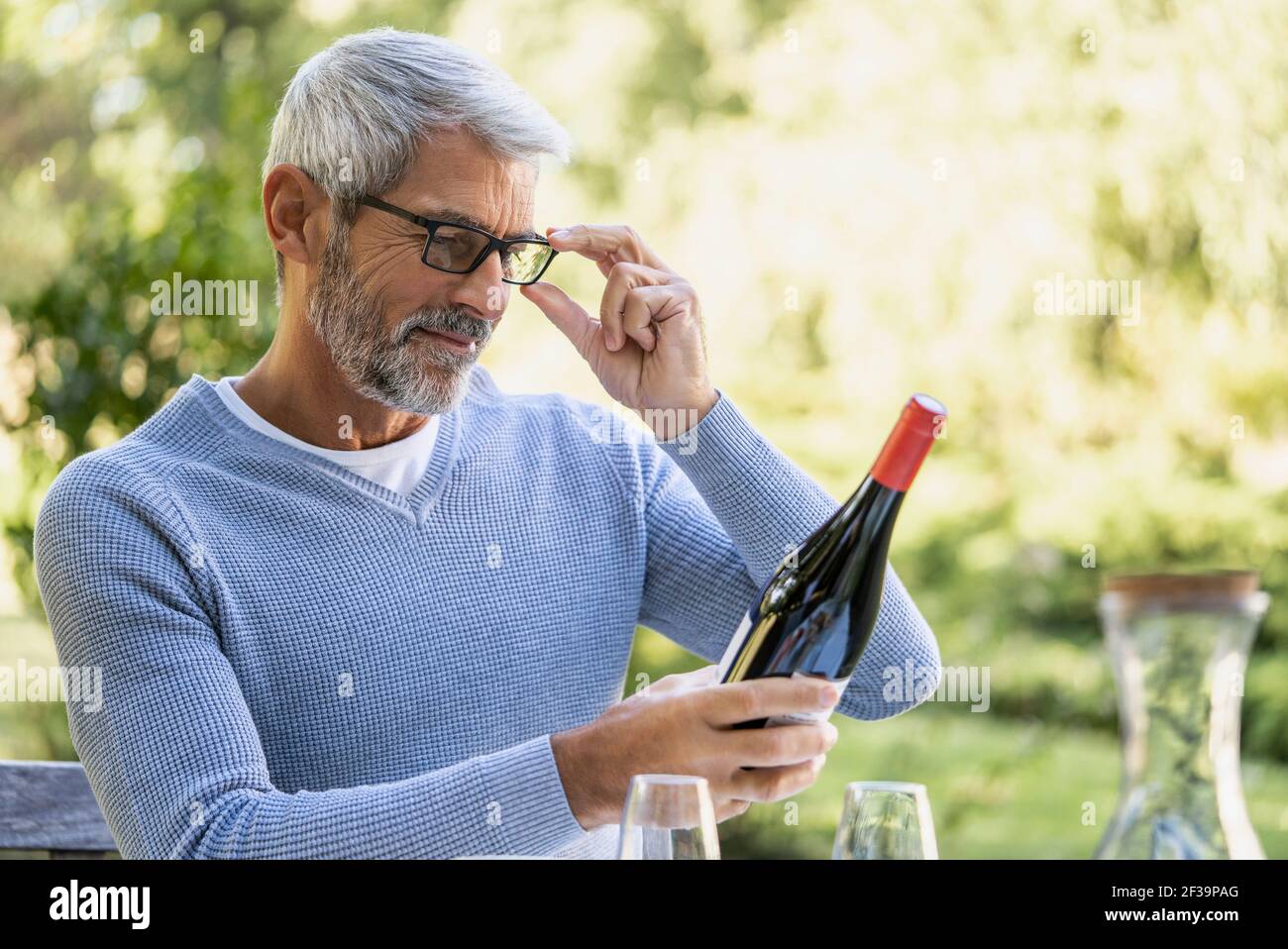 Mature man looking at wine bottle while sitting on chair Stock Photo