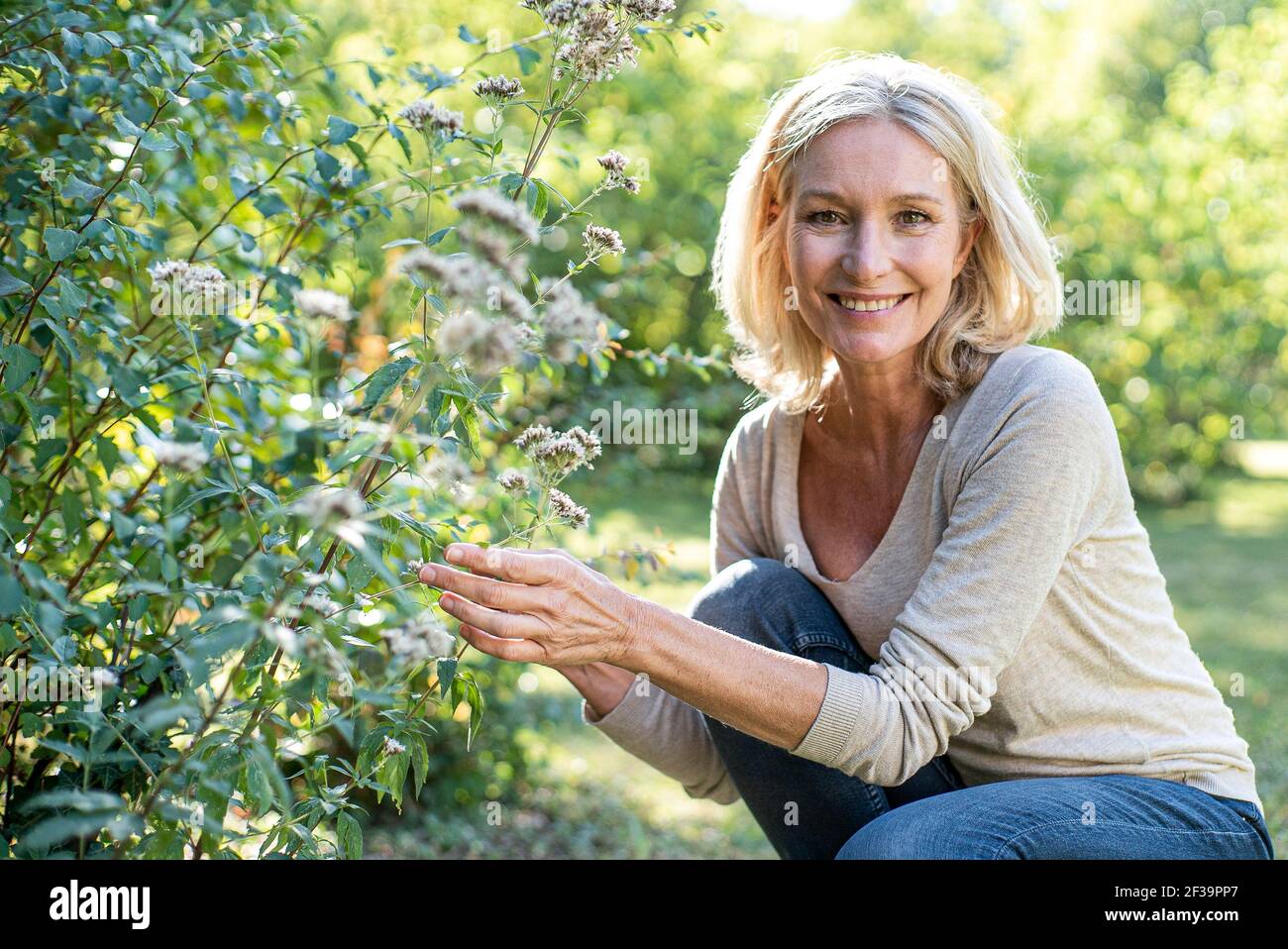 Portrait of smiling mature woman touching plant in backyard Stock Photo