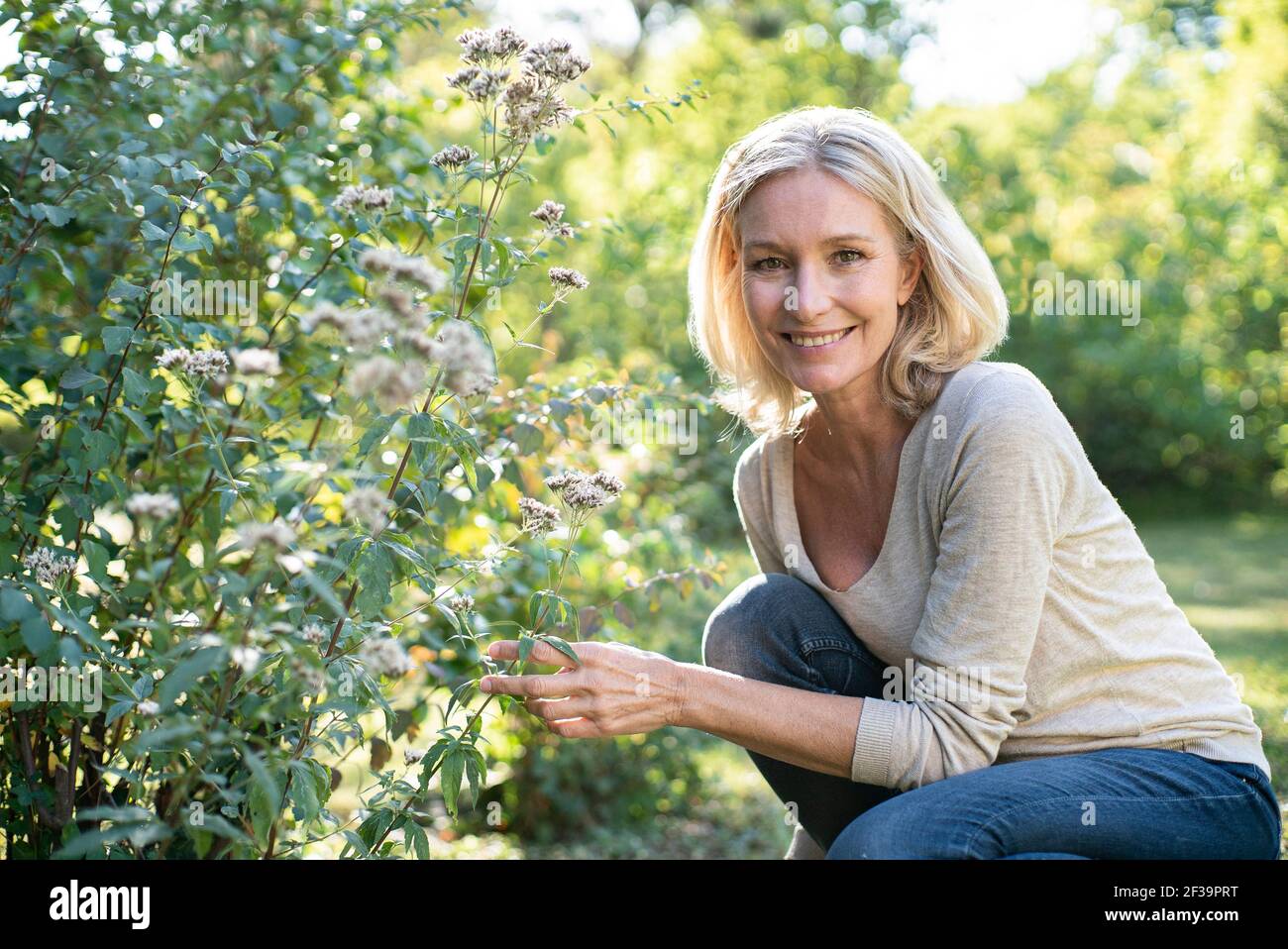 Portrait of smiling mature woman touching plant in backyard Stock Photo