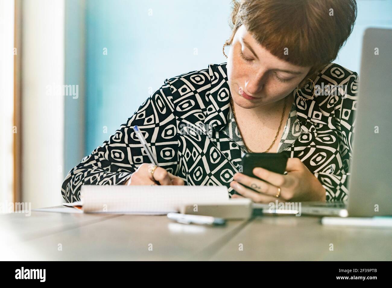 Woman using smartphone while writing in notepad at home Stock Photo