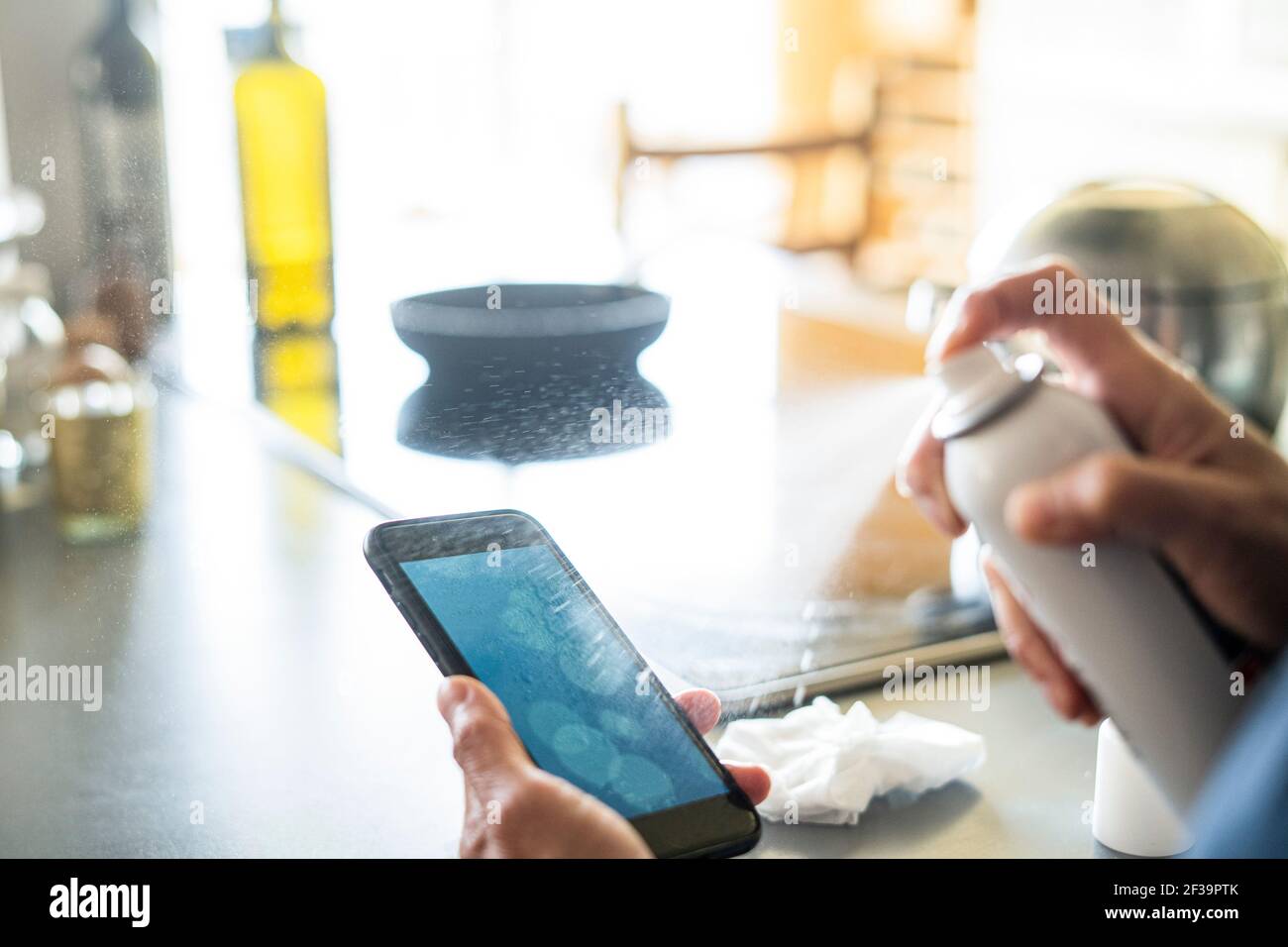 Close-up of woman's hands spraying disinfectant on smartphone at home Stock Photo