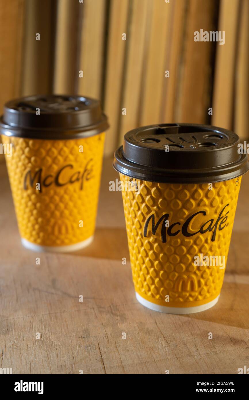 Ukraine, Kyiv - February 17, 2021: Yellow glass of coffee from McDonald's. Paper glass drink McCafe. offee cup on table with shadows. Menu in fastfood restaurant. Stock Photo