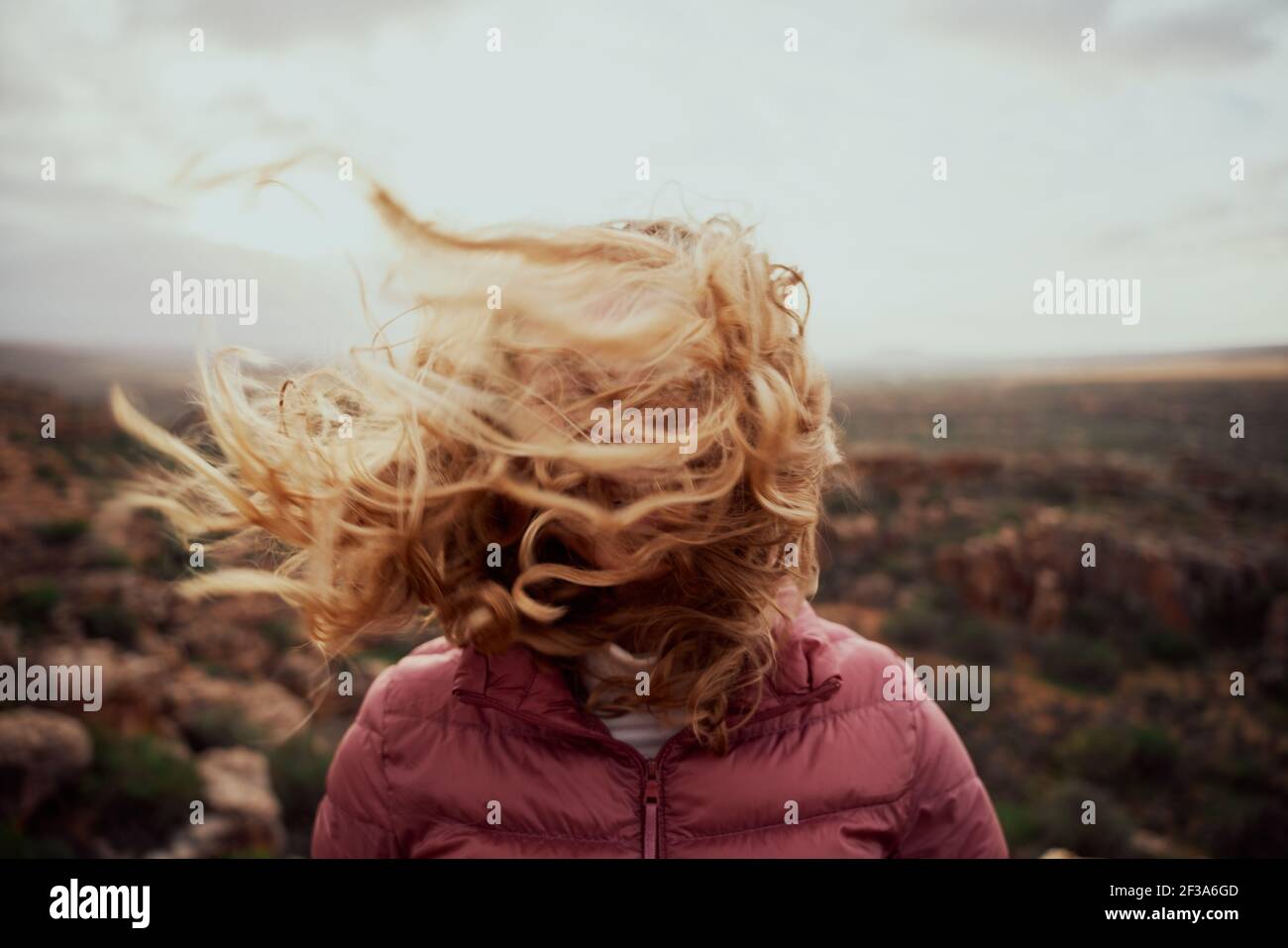 Closeup of young woman face covered with flying hair in windy day standing at mountain Stock Photo