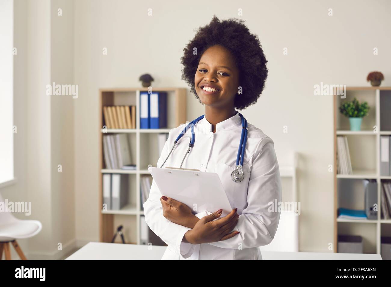 Portrait of happy young doctor standing in medical office, smiling and looking at camera Stock Photo