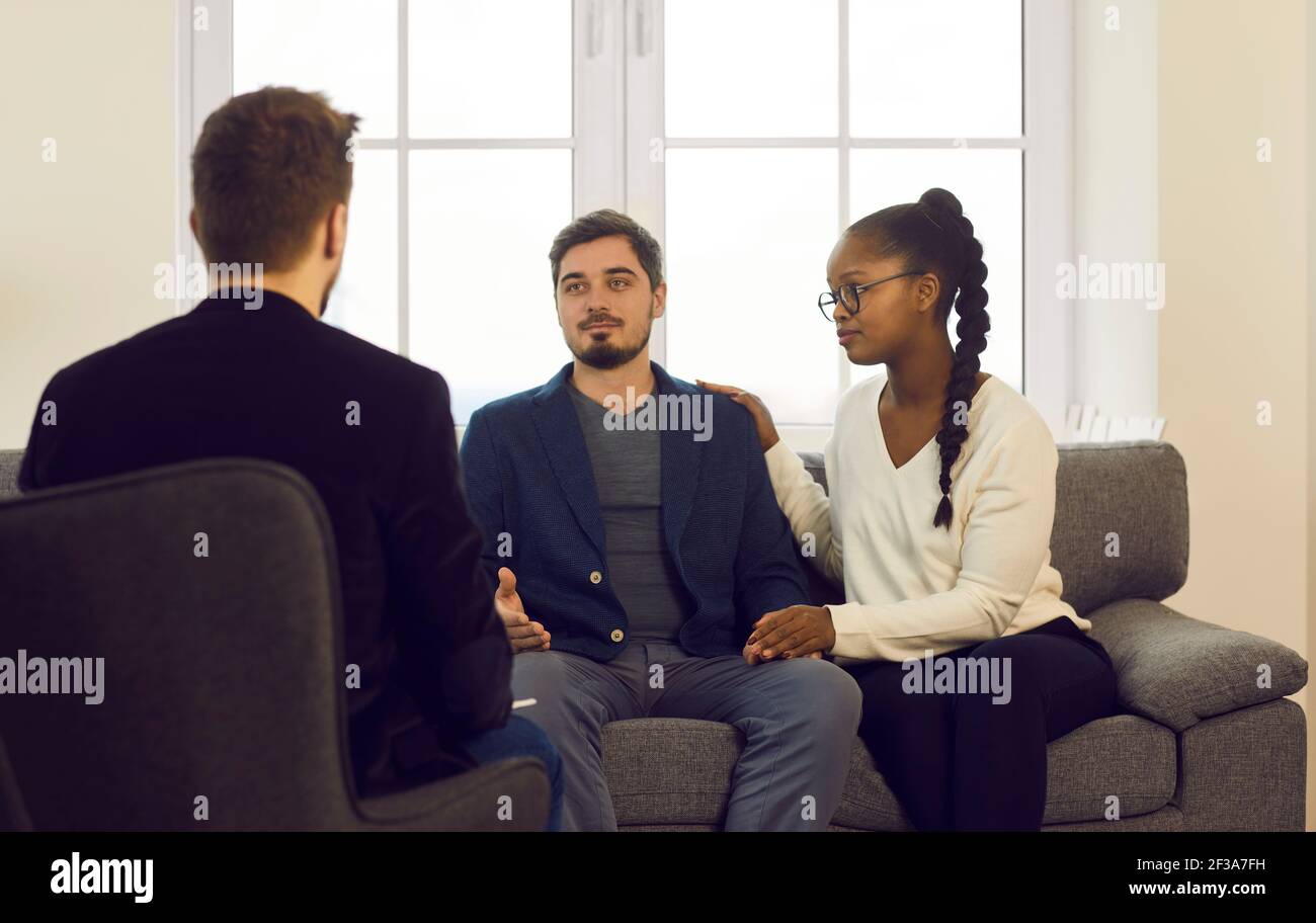 Young interracial spouses talking to man specialist at family consultation Stock Photo