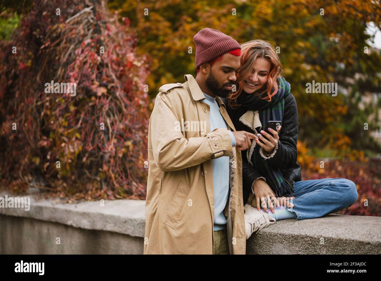 Multinational focused nice couple hugging and using mobile phone at ...